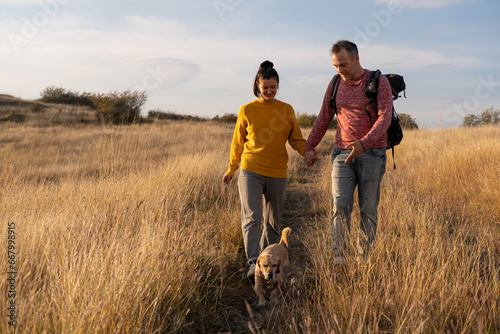 Young couple hiking through autumn fields and hills during warm day with their dog. Weekend, leisure, sport
