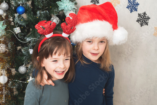 Two laughing girls stand near a Christmas tree in New Year's decor. Christmas holiday. Real people, simple life