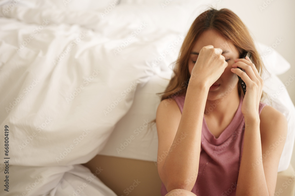 Unhappy asian woman sitting on bedroom floor, covering face with hand and using smartphone with worried expression at bedroom. Unhappy asian woman sitting on bedroom floor, covering face with hand and using smartphone with worried expression at bedroom.