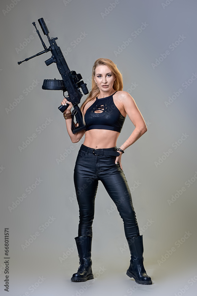 slender beautiful woman in a black leather suit with a machine gun in her hands on a gray background slender beautiful woman in a black leather suit with a machine gun in her hands on a gray background