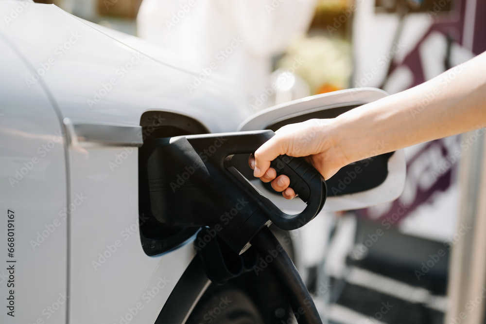 Obraz premium Hand plugging in a charger in an electric car socket.Electric car or ev is charging at station..