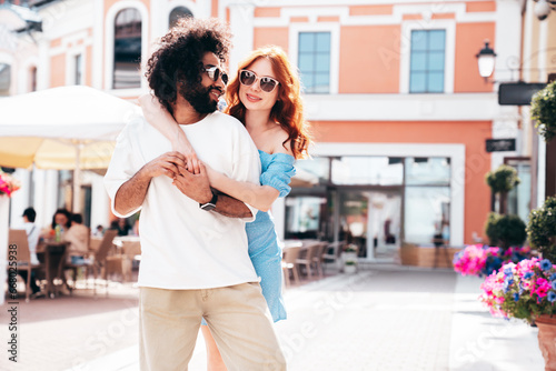 Smiling beautiful redhead woman and her handsome boyfriend. Model in casual summer clothes. Happy cheerful family. Female having fun. Couple posing in the street at sunny day. In sunglasses