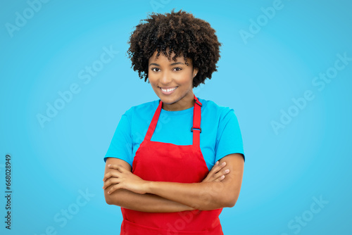 Beautiful laughing african american waitress with red apron on blue background
