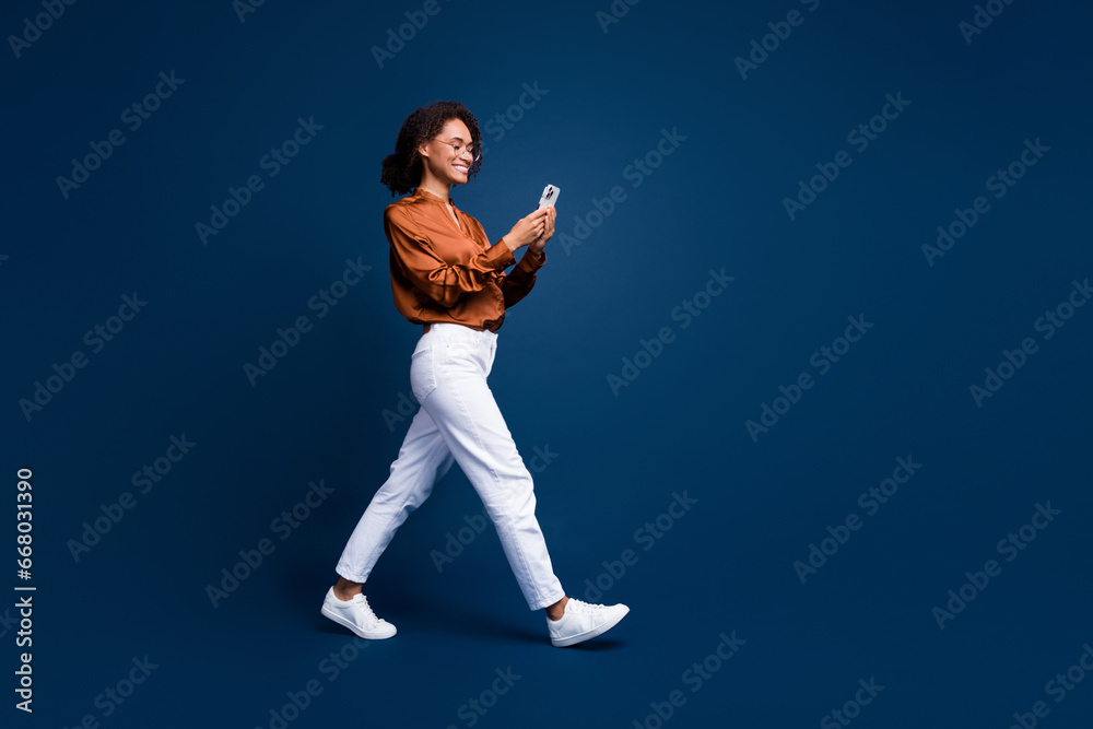 © deagreez - Full length photo of good mood cute lady wear silk brown shirt spectacles texting modern device empty space isolated blue color background
