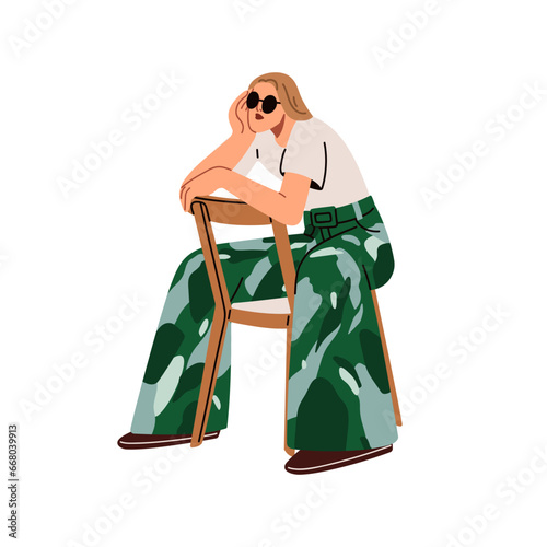 Fashion girl sitting, leaning on chair back. Modern young woman in sunglasses...