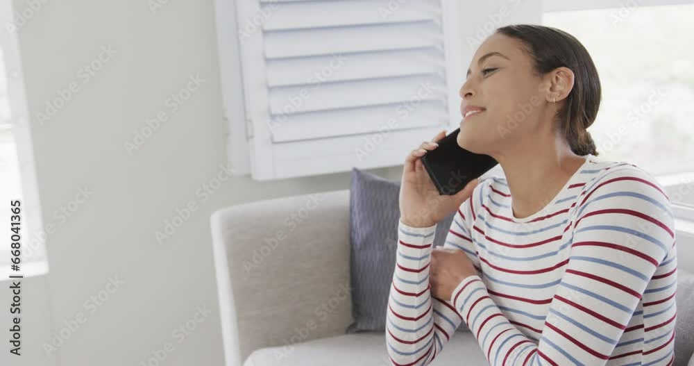 Happy biracial woman sitting on sofa talking on smartphone, copy space, slow motion Happy biracial woman sitting on sofa talking on smartphone, copy space, slow motion