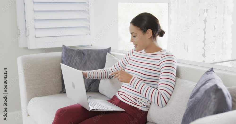 Happy biracial woman sitting on sofa using laptop for online shopping, slow motion Happy biracial woman sitting on sofa using laptop for online shopping, slow motion