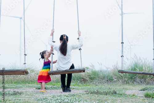 A young mother and her lovely little daughter are at a windmill field.