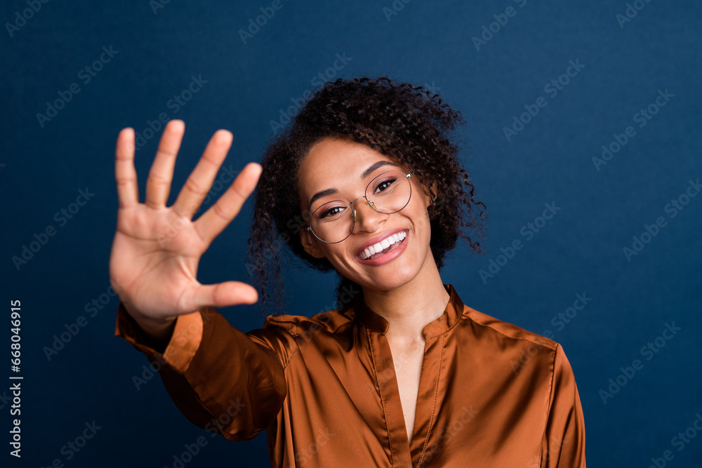 Photo of friendly excited lady wear silk brown shirt spectacles waving arm palm hello isolated blue color background Photo of friendly excited lady wear silk brown shirt spectacles waving arm palm hello isolated blue color background