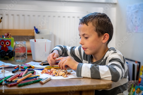 child preparing for schoolwork. the boy sewing crayons. he is sitting bihind floor sitting desk. photo