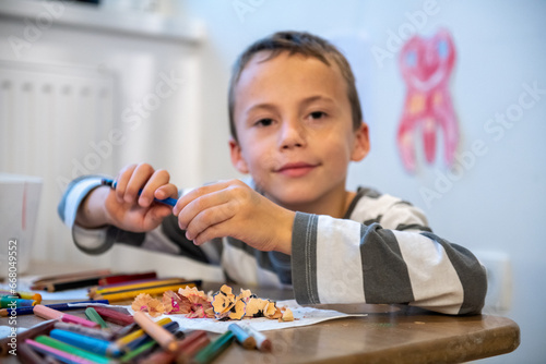 child preparing for schoolwork. the boy sewing crayons. he is sitting bihind floor sitting desk.