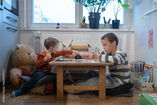 two children draw with crayons. they are sitting at the table. They are getting ready for school.