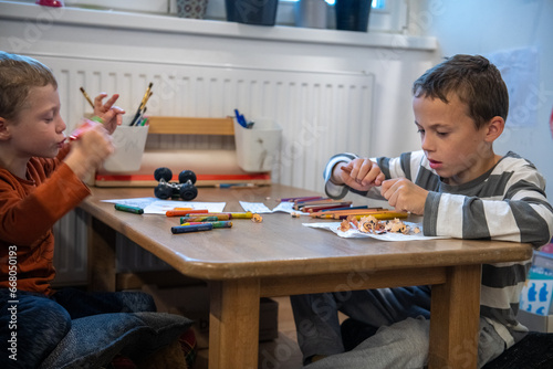 two children draw with crayons. they are sitting at the table. They are getting ready for school.
