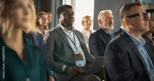 Black Man Sitting in a Crowded Audience at a Business Conference. Corporate Delegate Using Laptop Computer While Listening to an Inspirational Entrepreneurship Presentation About Developing Markets.