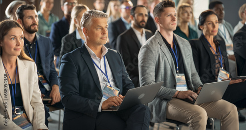 Caucasian Male Pharmaceutical CEO Sitting In Diverse Crowd At Medical Summit And Using Laptop Computer. Successful Man Listening To Presentations About New Developments In Biopharma and Medicine. photo