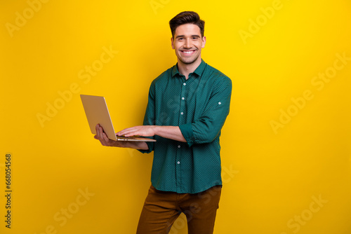 Photo of handsome nice man it specialist wear green stylish clothes hand hold netbook macbook isolated on yellow color background