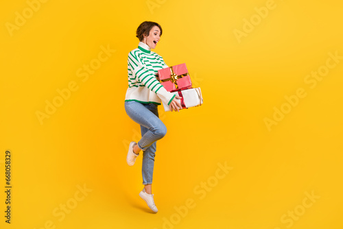Full body size photo of young positive jump girl wear sweater hold pile gift box packages anniversary isolated on yellow color background