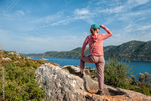 Beautiful traveler woman on mountain peak looking at the sea water in summer. Back pose