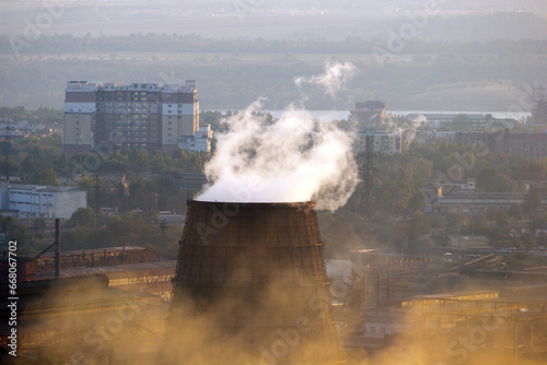 Cooling tower with steam coming out and city residental buildings on background