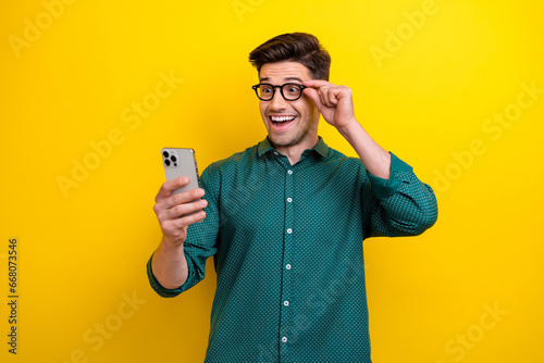 Photo of funky cheerful man wear green stylish clothes hold glasses read social media post coment isolated on yellow color background photo