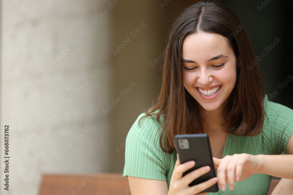 Happy woman using smart phone alone on a bench Happy woman using smart phone alone on a bench