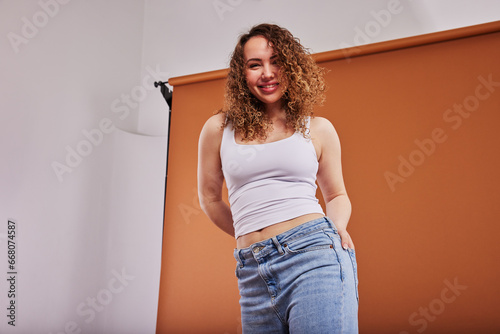 Young redheaded woman smiling while posing against an orange studio backdrop photo