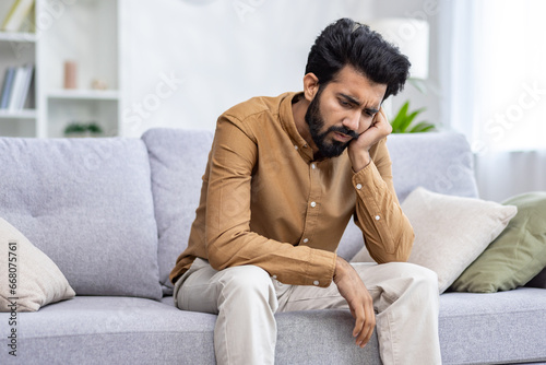 Sad depressed man sitting at home on sofa in living room, hopelessly lonely. photo