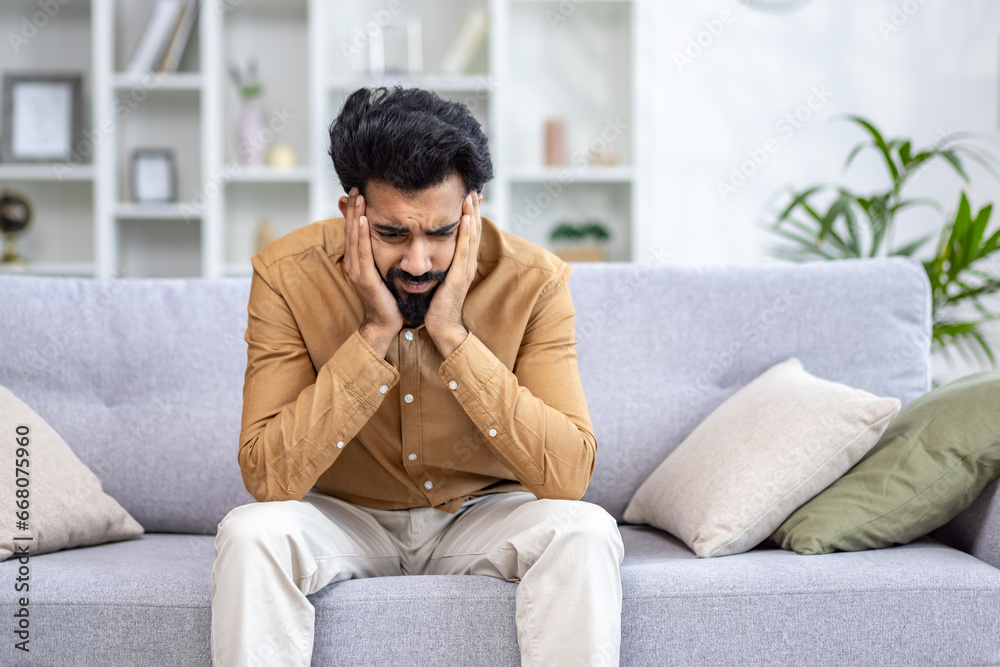 Sad depressed man sitting at home on sofa in living room, hopelessly lonely. Sad depressed man sitting at home on sofa in living room, hopelessly lonely.