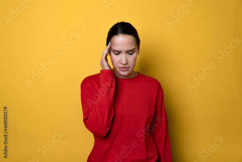 Sick ill sad tired young pretty woman wears red long sleeves put hand on head rub temples having headache suffering from migraine isolated on plain yellow background studio portrait