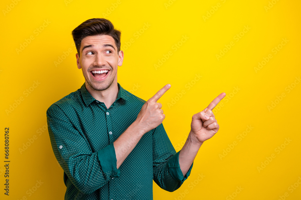 Photo of excited positive man wear green trendy clothes presenting empty space look up banner news isolated on yellow color background