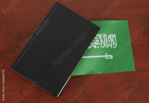 Saudi Arabia legal and law concept, with book on table and Saudi Arabia flag. The Arabic inscription on the flag: "There is no god but God: Muhammad is the Messenger of God."