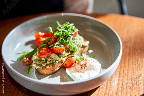 Open brioche sandwich with mint avocado, poached egg served with arugula and cherry tomato. Healthy breakfast. Toast with guacamole, vegetable and poached egg and eggs benedict with brioche