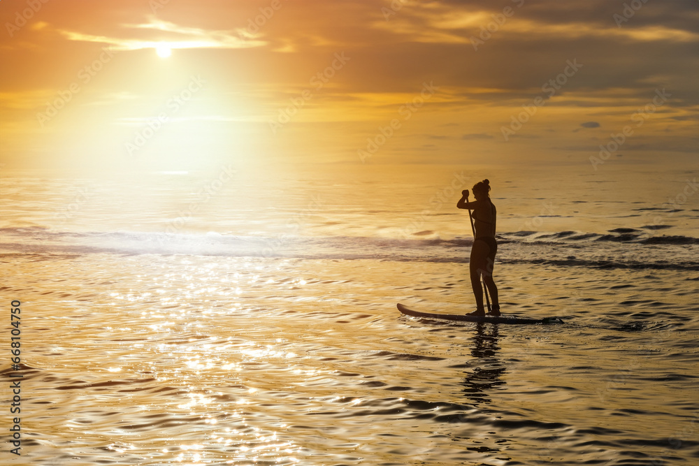 Pretty young girl doing paddle boarding in a beautiful lagoon at sunset
