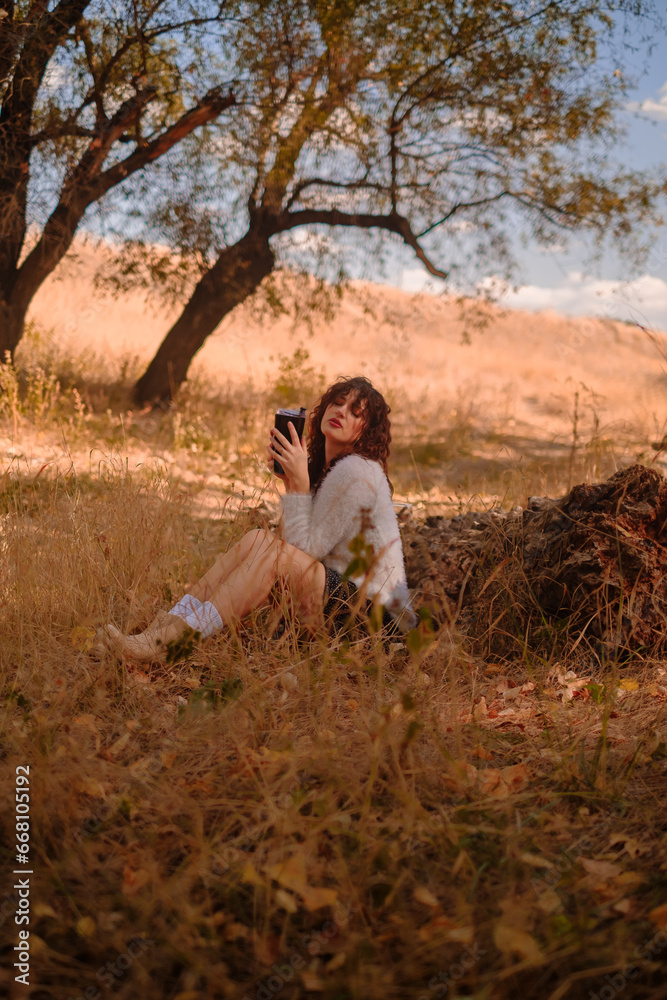 young woman relaxing outdoors on an autumn day, traveling to the forest, sitting on a wooden log in the forest and drinking hot tea, unity with nature, searching for the meaning of life young woman relaxing outdoors on an autumn day, traveling to the forest, sitting on a wooden log in the forest and drinking hot tea, unity with nature, searching for the meaning of life