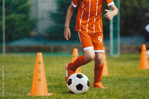 Children practicing dribbling at soccer pitch. Young boy running soccer ball in slalom drill between training cones