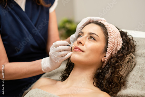 Anonymous beautician injecting filler into lips of female client