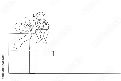 Continuous one line drawing young energetic astronaut sitting on giant gift box holding laptop raise one hand. Awesome space gift. Cosmonaut outer space. Single line draw design vector illustration