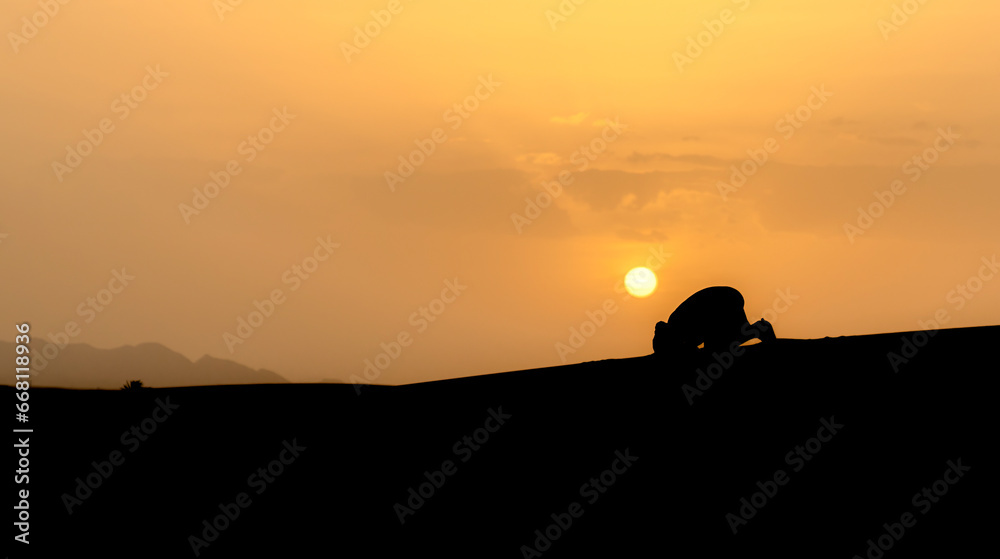 Silhouette of unidentified muslim Berber man praying on sand dunes at beautiful sunset in Sahara Desert, Morocco - obrazy, fototapety, plakaty 