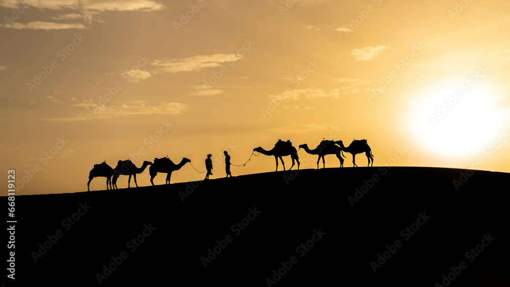Silhouette of two Berber men leading camel caravans come across each other on sand dunes during sunset in Sahara Desert, Morocco Silhouette of two Berber men leading camel caravans come across each other on sand dunes during sunset in Sahara Desert, Morocco