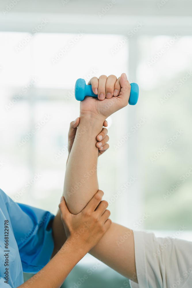 Physical therapist giving exercise by maintaining dumbbells on the arms and shoulders of a male patient. Physical therapy concept