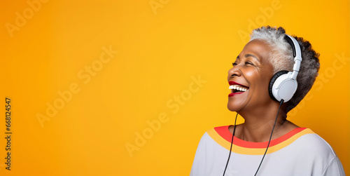 Studio portrait of mature black woman listening on headphones and laughing, yellow background	
 photo