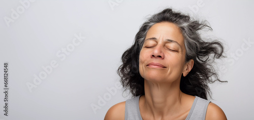Close up studio portrait of mature middle aged woman with eyes closed, natural look, positive self image, gray background