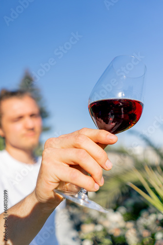 Photos A young charming man holds out a glass of wine to the camera and carefully exami