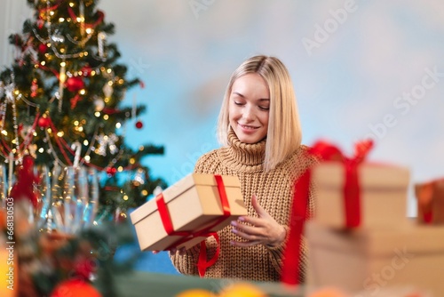 A young woman holds a New Year's gift with a red ribbon in her hands. Close-up of a woman holding a Christmas gift box with a red ribbon. Holidays concept. A young girl in a white sweater holds a New