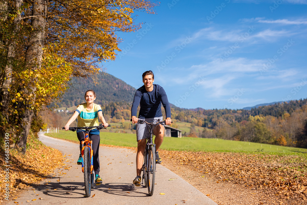 Young happy couple cycling downhill along the autumn forest trail, holding hands and having fun in the ride. Nature, fun, relaxation, and active lifestyles concepts. Young happy couple cycling downhill along the autumn forest trail, holding hands and having fun in the ride. Nature, fun, relaxation, and active lifestyles concepts.
