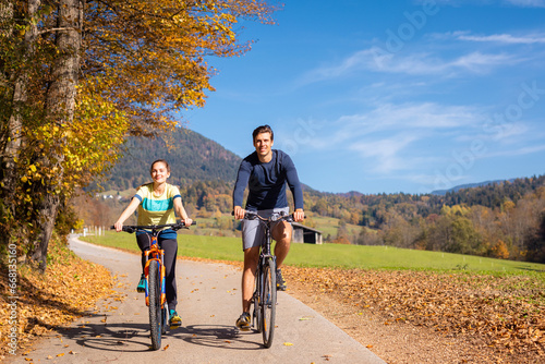 Young happy couple cycling downhill along the autumn forest trail, holding hands and having fun in the ride. Nature, fun, relaxation, and active lifestyles concepts.