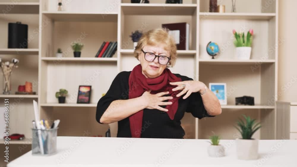 old woman sitting at the table clutches her chest with her hands and begins massaging during a heart attack old woman sitting at the table clutches her chest with her hands and begins massaging during a heart attack