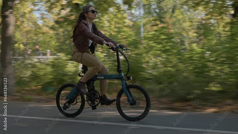 Stylish young woman riding an electric bicycle in city centre in the park during fall season. Concept of cycling sport activity and eco transportation by bike Stylish young woman riding an electric bicycle in city centre in the park during fall season. Concept of cycling sport activity and eco transportation by bike