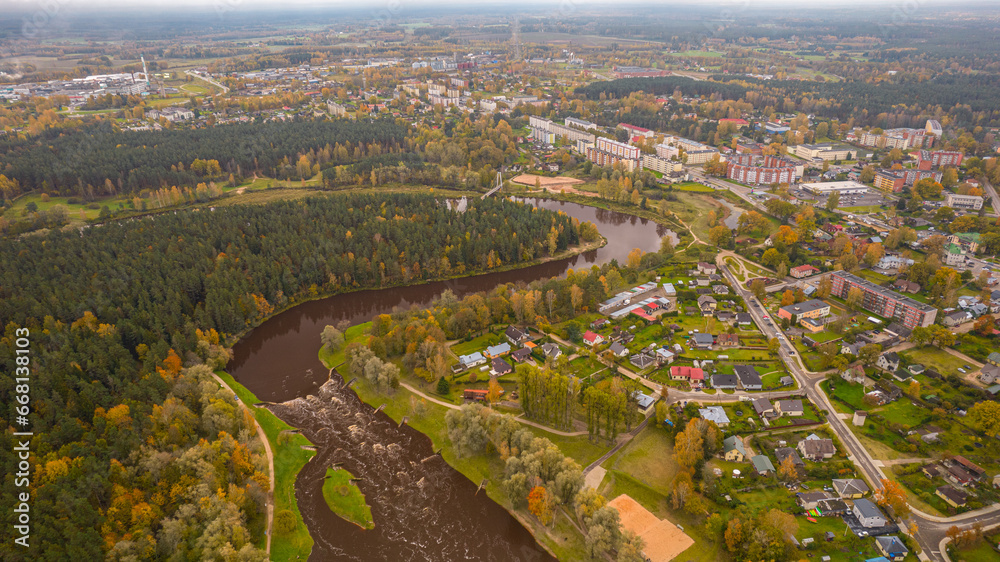 Obraz premium City of Valmiera from above in autumn. Panoramic Fall Landscape with Cityscape, Clouds, and Foliage. Cityscape with autumn foliage, flowers, and a tree in high angle view.
