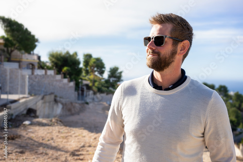 Portrait of handsome man wearing elegant white sweater and sunglasses, standing in the nature